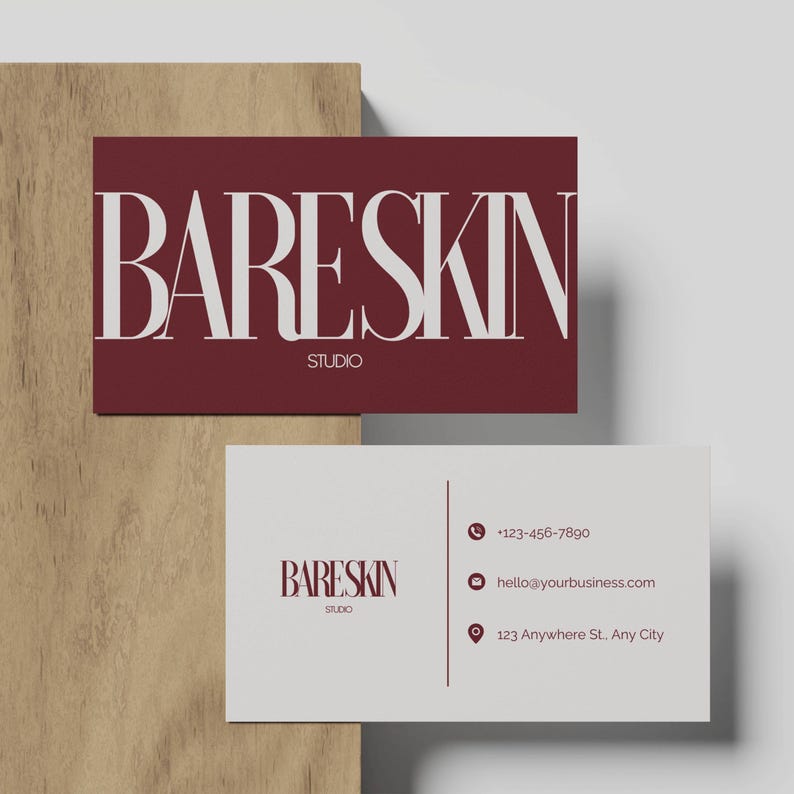 K&ouml;nnte beinhalten: Zwei Visitenkarten. Eine zeigt den Text "BARESKIN STUDIO" in Wei&szlig; auf burgunderrotem Hintergrund, die andere ist wei&szlig; mit Kontaktdaten. Die Karten werden auf einer Holzoberfl&auml;che pr&auml;sentiert.