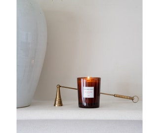 Puede incluir: Una vela de vidrio marrón con una etiqueta blanca que dice "Cire Trudon" y "Nuit de Longchamp" en un apagador de velas dorado.