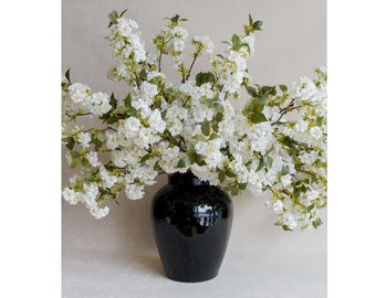 May include: A black ceramic vase with a glossy finish filled with white cherry blossoms.