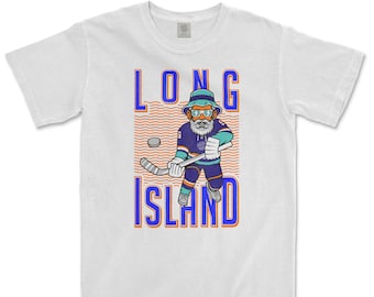 Op de afbeelding: Wit T-shirt met een cartoonillustratie van een hockeyer die een blauw en turquoise shirt, een zonnebril en een hoed draagt. De tekst "LONG ISLAND" is in blauw en oranje gedrukt.