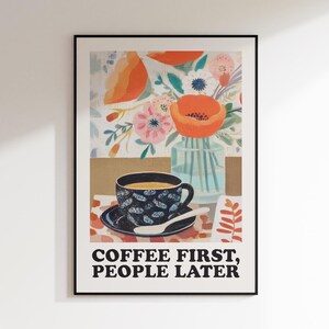 May include: Framed art print featuring a coffee cup on a saucer with a spoon, set against a floral background. The print includes the text "COFFEE FIRST, PEOPLE LATER" in bold, black letters.