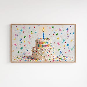 May include: A framed painting of a two-tiered birthday cake with white frosting and colorful sprinkles. The cake has the words "HAPPY BIRTHDAY" in colorful letters. A blue candle with a lit flame sits atop the cake. The background is white with colorful paint strokes.