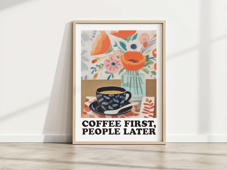 May include: A framed art print featuring a coffee cup and flowers. The cup and saucer are navy blue with a floral pattern. The print includes the text "COFFEE FIRST, PEOPLE LATER". The background includes a vase of flowers and a floral pattern.