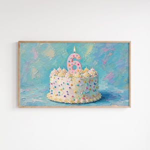 Op de afbeelding: Een ingelijste rechthoekige wandkunstprint met een impasto olieverfschilderij van een witte verjaardagstaart met kleurrijke hagelslag en een enkele roze kaars in de vorm van het cijfer zes tegen een textuurrijke lichtblauwe achtergrond.