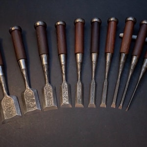 May include: A set of woodworking chisels with dark wooden handles and silver blades. The chisels are displayed in a row, with different blade shapes and sizes, suitable for fine woodworking tasks.