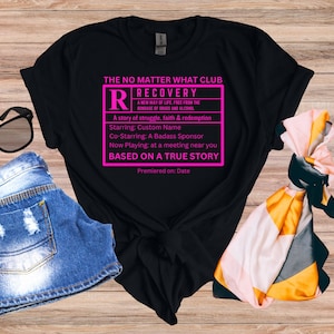 May include: Black t-shirt with a pink graphic that reads "The No Matter What Club" and features a movie rating style box with the text "Recovery" and "Based on a True Story".