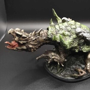 May include: A detailed, hand-painted miniature of a green and brown turtle-like creature with a spiky tail and a large, open mouth. The creature is posed on a black base with a rocky texture.