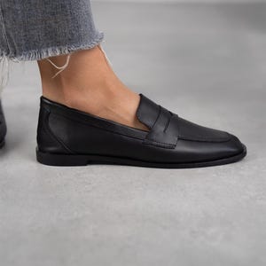 May include: Black leather loafers with a penny strap detail. The loafers have a rounded toe and a low heel.