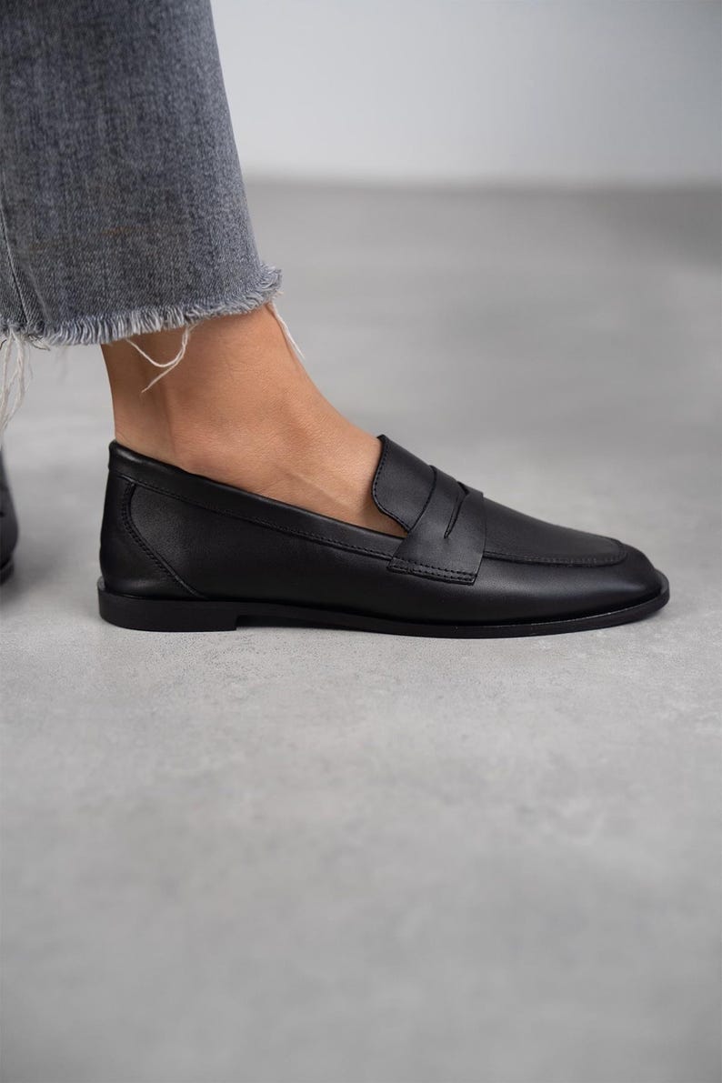 May include: Black leather loafers with a penny strap detail. The loafers have a rounded toe and a low heel.