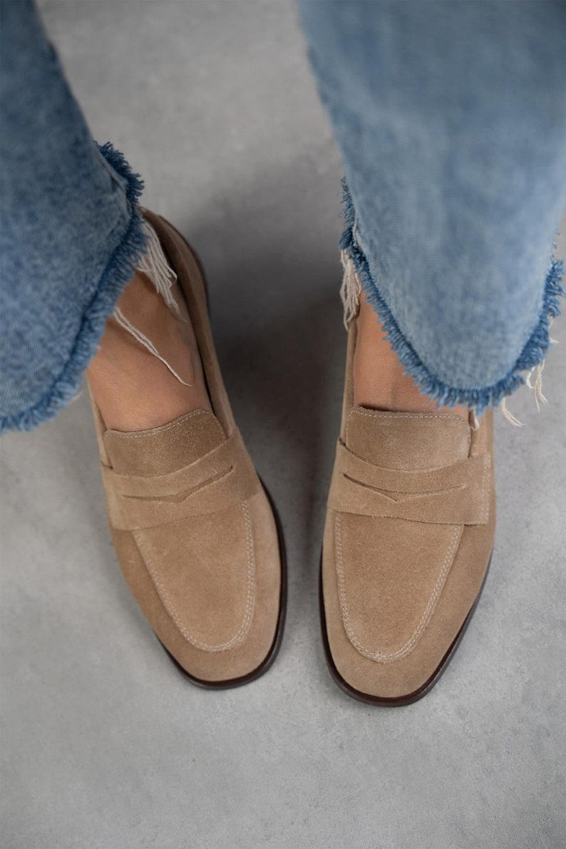 May include: A pair of light brown suede loafers with a simple design. The loafers have a rounded toe and a low heel.