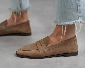 May include: A pair of brown suede loafers with a simple design. The loafers have a rounded toe and a low heel.