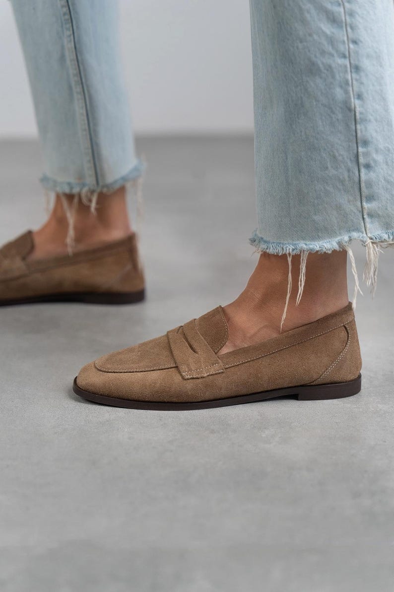 May include: A pair of brown suede loafers with a simple design. The loafers have a rounded toe and a low heel.