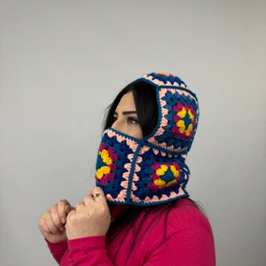 May include: A crocheted hooded face mask with a geometric pattern in shades of pink, blue, yellow, and purple.