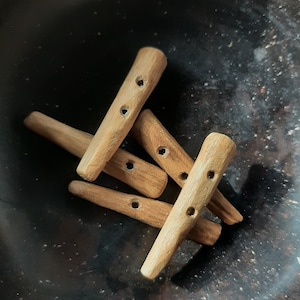 Könnte beinhalten: Fünf Holz-Knöpfe mit jeweils zwei Löchern. Die Knöpfe liegen auf einer dunklen Oberfläche in einem Stapel.