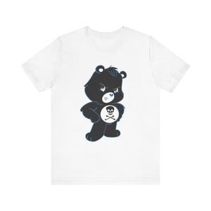 May include: A white t-shirt featuring a black and blue cartoon bear wearing a blue heart and a skull and crossbones on its chest.