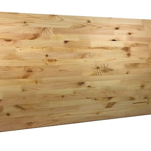 Pode incluir: Uma peça grande e retangular de madeira não acabada, de cor clara. A madeira tem um padrão de grão natural e é composta por várias tábuas.