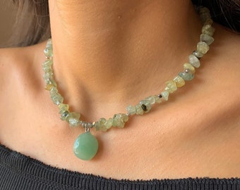 May include: A green stone necklace with a large green stone pendant. The necklace is made of small, irregular green stones.