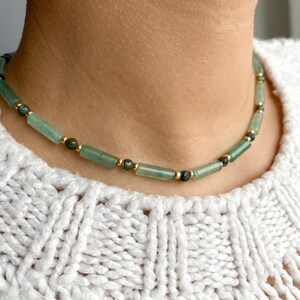 Pode incluir: Um colar choker de contas verdes e douradas. O colar &eacute; feito de pequenas pedras verdes retangulares e contas douradas.