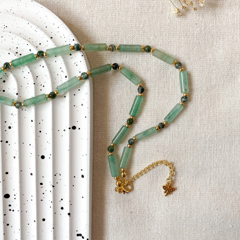 Pode incluir: Um colar verde e dourado com uma corrente delicada e um fecho de borboleta. O colar &eacute; feito com contas de pedra verde e espa&ccedil;adores dourados.