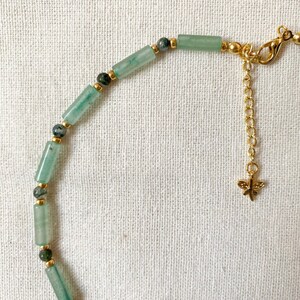 Pode incluir: Um bracelete de contas verdes e douradas com um fecho de lib&eacute;lula. O bracelete &eacute; feito com pequenas contas verdes cil&iacute;ndricas e espa&ccedil;adores dourados. O fecho de lib&eacute;lula est&aacute; preso a uma corrente dourada.