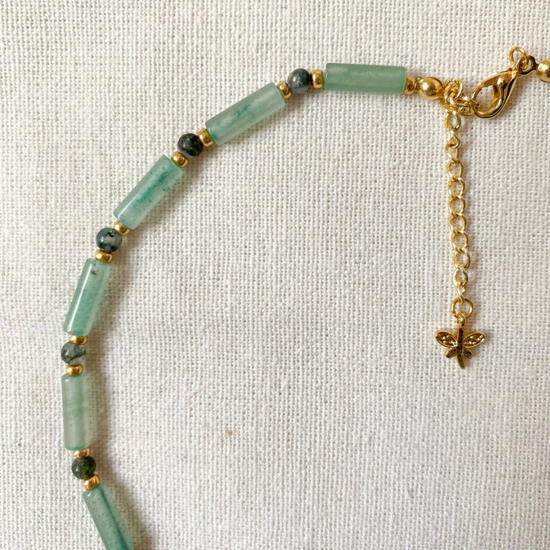 Pode incluir: Um bracelete de contas verdes e douradas com um fecho de lib&eacute;lula. O bracelete &eacute; feito com pequenas contas verdes cil&iacute;ndricas e espa&ccedil;adores dourados. O fecho de lib&eacute;lula est&aacute; preso a uma corrente dourada.