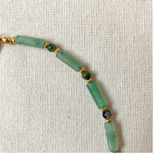 Pode incluir: Um bracelete de contas verdes e douradas com contas redondas e retangulares.