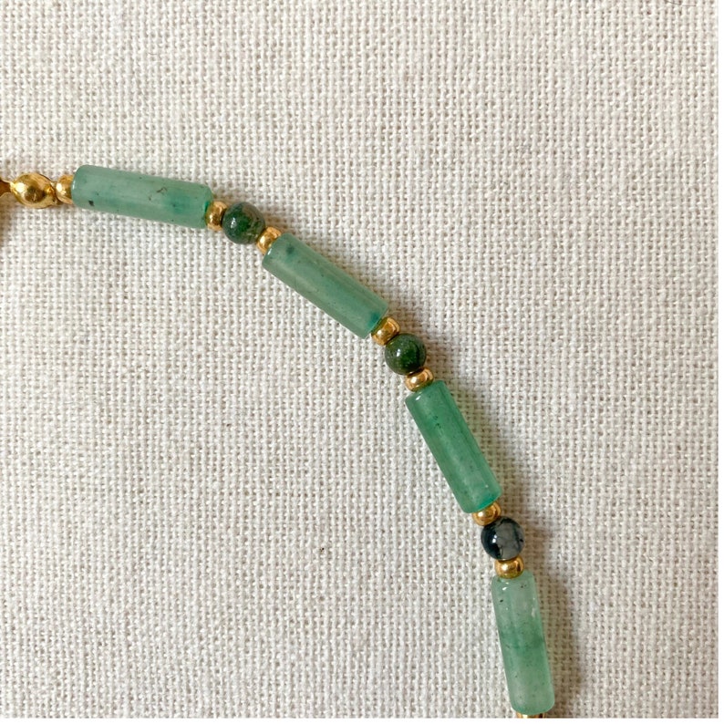 Pode incluir: Um bracelete de contas verdes e douradas com contas redondas e retangulares.