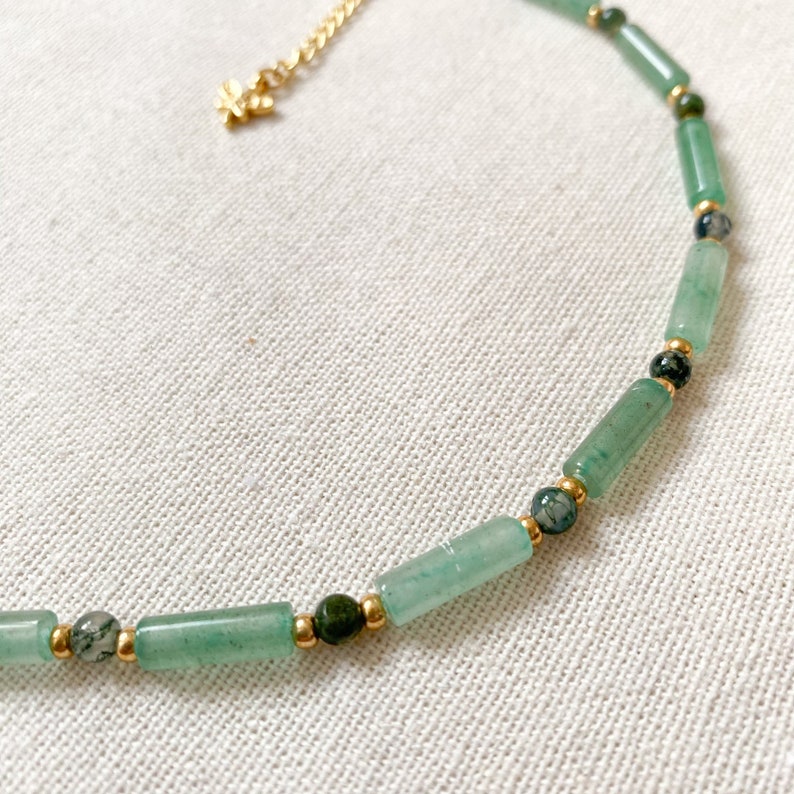 Pode incluir: Um colar de contas verdes e douradas com um pequeno fecho dourado. O colar &eacute; feito com contas de pedra verde e espa&ccedil;adores dourados.