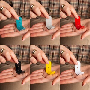 Puede incluir: Seis ganchos de metal de diferentes colores para colgar objetos en una pared. Los ganchos son de varios colores, incluyendo azul, gris, rojo, negro, amarillo y blanco.