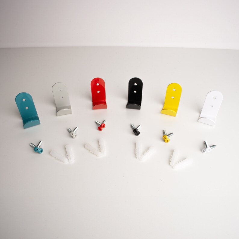 Puede incluir: Un conjunto de seis ganchos met&aacute;licos de varios colores, incluyendo azul, plateado, rojo, negro, amarillo y blanco. Los ganchos est&aacute;n dispuestos en una fila sobre una superficie blanca, con peque&ntilde;os anclajes de pl&aacute;stico blanco y tornillos esparcidos alrededor.