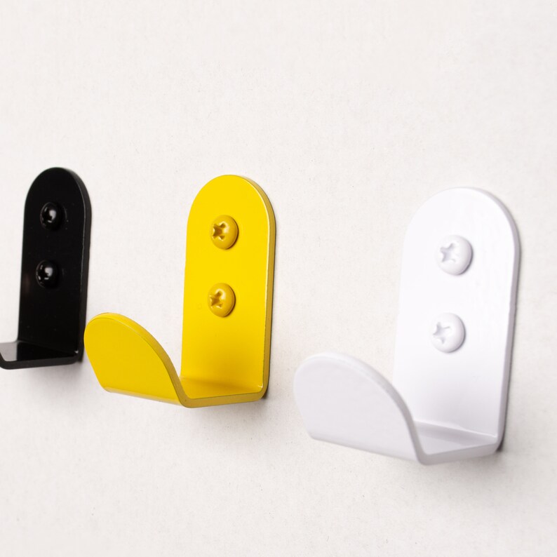 Puede incluir: Tres ganchos de pared en negro, amarillo y blanco. Cada gancho tiene dos tornillos para montaje.