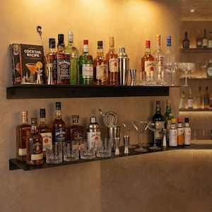 Puede incluir: Una barra de bar en casa con dos estantes negros que exhiben varias botellas de licor, mezcladores de cócteles, cocteleras y cristalería. Un libro de recetas de cócteles es visible en el estante superior.