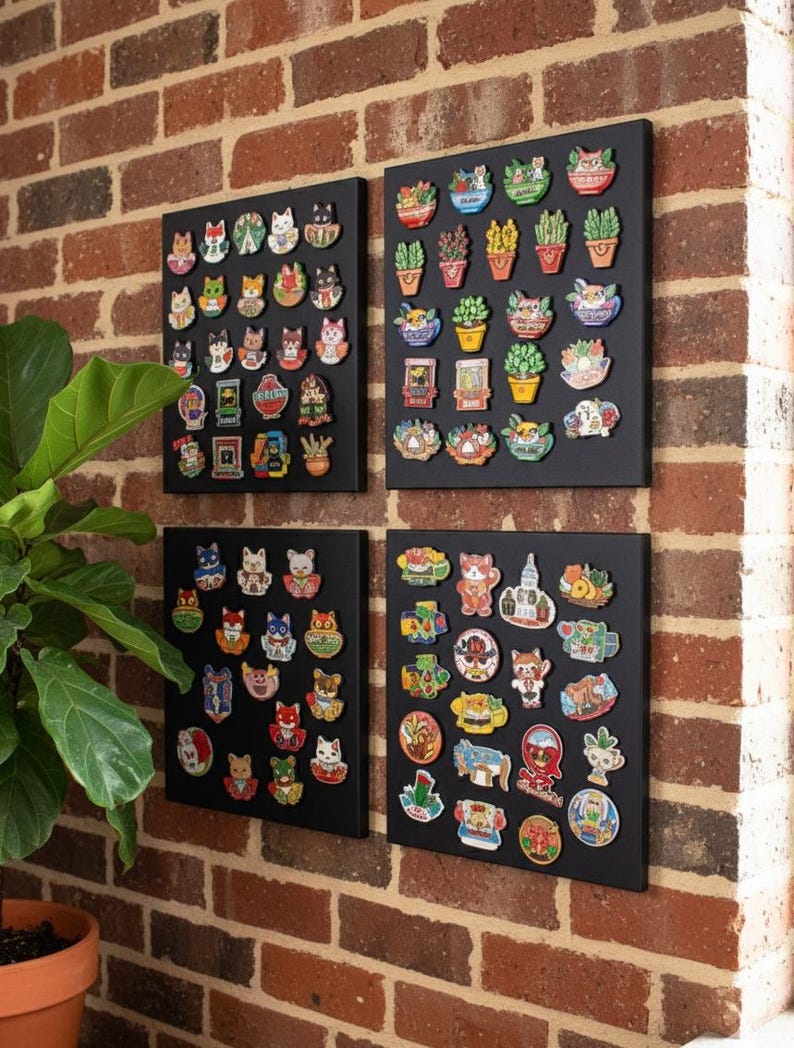 May include: Four black display boards mounted on a brick wall, each covered with colorful enamel pins. The pins feature cat and plant designs, showcasing a variety of colors and styles. The boards are arranged in a square formation.