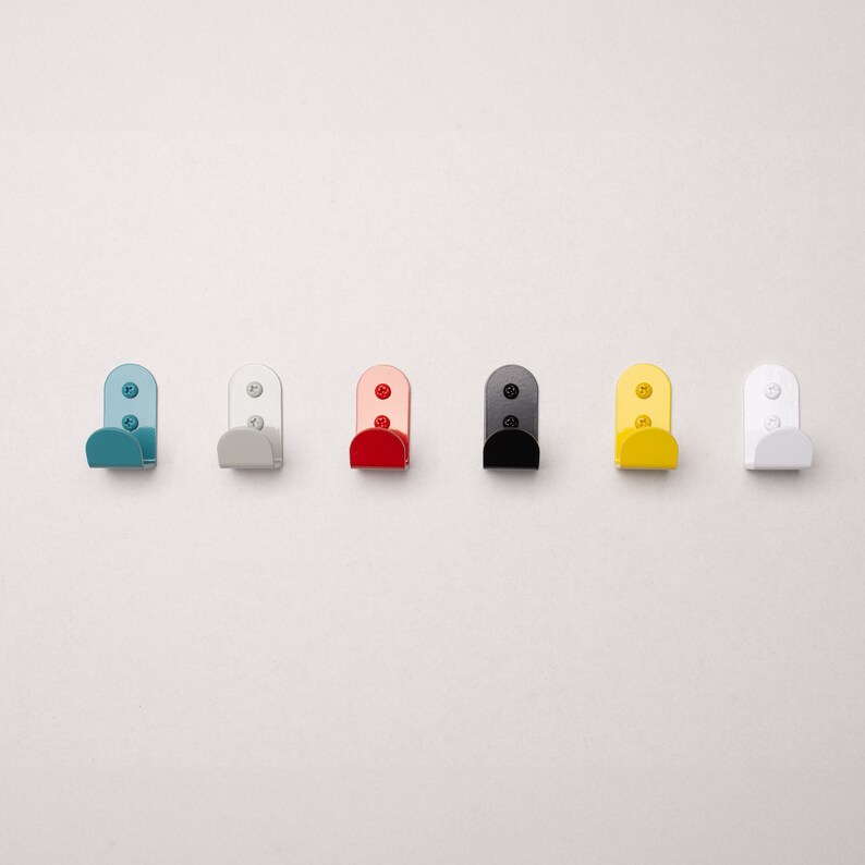 Puede incluir: Siete peque&ntilde;os ganchos de metal en diferentes colores: azul claro, gris, rojo, negro, amarillo y blanco. Los ganchos son todos del mismo tama&ntilde;o y forma, y est&aacute;n dispuestos en una fila.