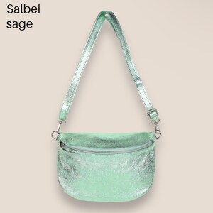 May include: A light green metallic crossbody bag with a silver zipper and adjustable strap. The bag has a slightly curved shape and a textured finish.