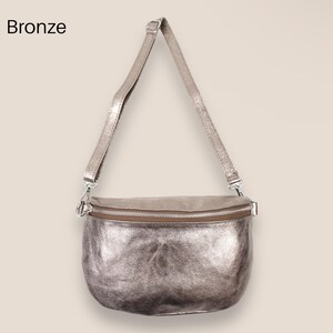 May include: A silver metallic leather crossbody bag with a zipper closure. The bag has a long adjustable strap.