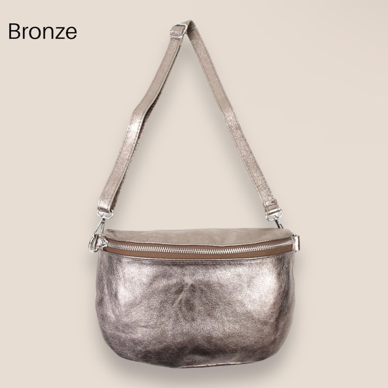 May include: A silver metallic leather crossbody bag with a zipper closure. The bag has a long adjustable strap.