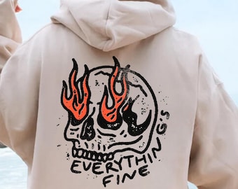 Könnte beinhalten: Ein beiger Hoodie mit einem Totenkopf-Motiv und dem Text "EVERYTHING FINE" auf der Rückseite. Der Totenkopf hat Flammen als Augen.