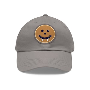 May include: A gray baseball cap with a brown patch featuring a smiling face with blue eyes and a row of white teeth.