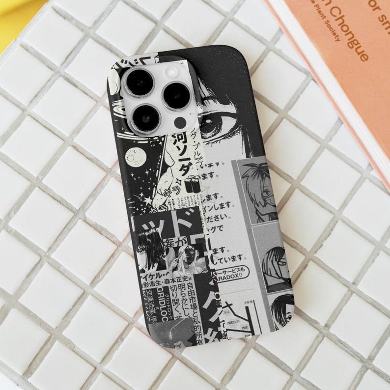 May include: Black and white phone case featuring a manga-style collage. The design includes panels with Japanese text, manga illustrations, and a large eye graphic. The case is on a white tiled surface.