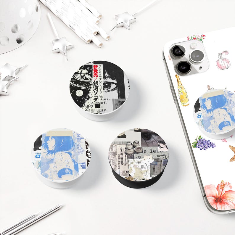 May include: A collection of round phone grips with various designs. One features a manga-style eye and text, another a blue-toned anime illustration, and the third a collage of images and text. A phone with a matching grip is also visible.