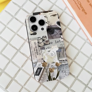 May include: A clear phone case featuring a collage of newspaper clippings, illustrations, and a cat design. The case includes a drawing of a woman's face, shoes, and text in Japanese. The case also has a floral design.