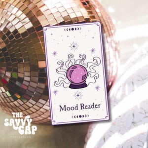 Könnte beinhalten: Eine weiße Karte mit einem violetten Rand und einer rosa Kristallkugel, aus der violetter Rauch aufsteigt. Die Karte trägt den Text "Mood Reader" und ein Mondphasen-Symbol.