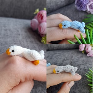 May include: Three miniature crocheted goose figurines in different colors: white, light blue, and gray. Each goose has a small black eye and an orange beak.