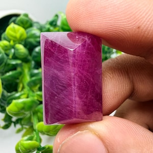 Peut inclure: Une pierre précieuse rectangulaire à facettes d'une couleur rose magenta profond avec une texture interne translucide et fibreuse. La pierre présente une surface supérieure plate avec des bords biseautés et une finition polie.