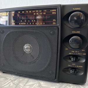 Peut inclure: Une radio noire Timex avec une grille de haut-parleur, un bouton de réglage, un bouton de volume et des boutons pour AM, FM, TV 1, TV 2/WB, marche/arrêt et alarme.