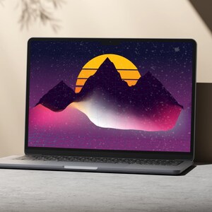 May include: A silver laptop displaying a retro-style digital art scene. The artwork features a yellow sun setting behind dark purple mountains, with a pink and white gradient in the foreground, set against a starry night sky.
