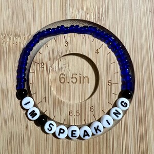 May include: A blue beaded bracelet with white beads spelling out "I'm Speaking". The bracelet is 6.5 inches in circumference.