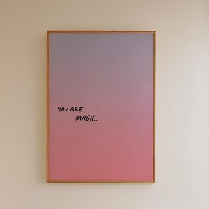 Może przedstawiać: Wnętrze łazienki z oprawionym dziełem sztuki przedstawiającym gradient różu i fioletu oraz napis "YOU ARE MAGIC". Drewniany stołek podtrzymuje tacę z butelką i szczotką. Widoczna jest również biała wanna i okno.