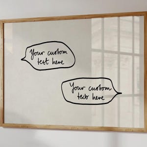 May include: A rectangular wall art piece featuring a light-colored background enclosed in a thin wooden frame. The artwork displays two hand-drawn black speech bubbles, each containing the handwritten text "Your custom text here" in black ink.
